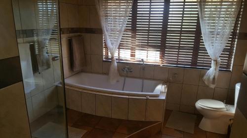 a bathroom with a tub and a toilet and a window at 12 On Vaal Drive Guesthouse in Vanderbijlpark