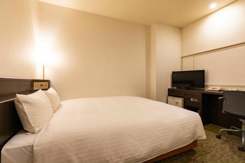 a hotel room with a white bed and a desk at Nishitetsu Inn Kurosaki in Kitakyushu