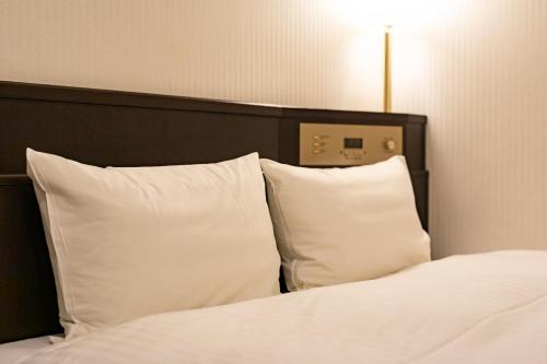 a bed with white pillows and a black headboard at Nishitetsu Inn Kurosaki in Kitakyushu