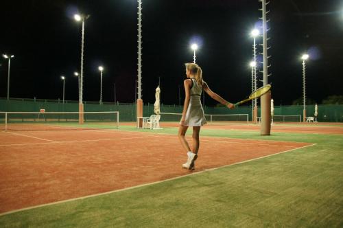 a woman holding a tennis racket on a tennis court at night at Cleopatra Luxury Resort Makadi Bay in Hurghada