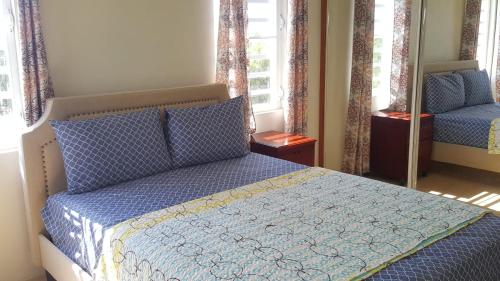 a bedroom with a bed with a blue comforter and two windows at White Sands Anguilla - Sea in Blowing Point Village