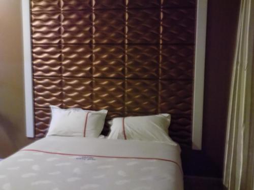 a bed with white pillows and a brown headboard at Freedom City Hotel Najjanankumbi Kamapala in Kampala