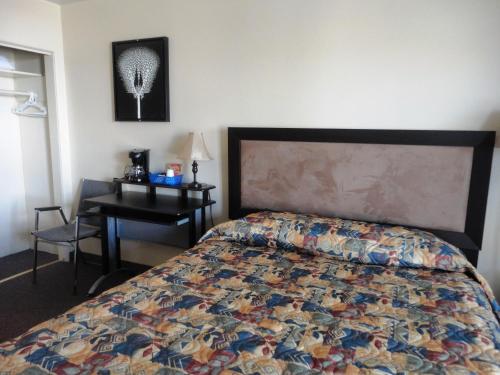 a bedroom with a bed and a desk with a bedspread at Stratford Motel in Whitehorse