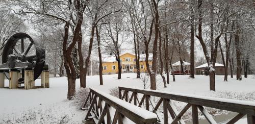 a wooden bridge in a snow covered park with a yellow house at Långshyttans Brukshotell in Långshyttan