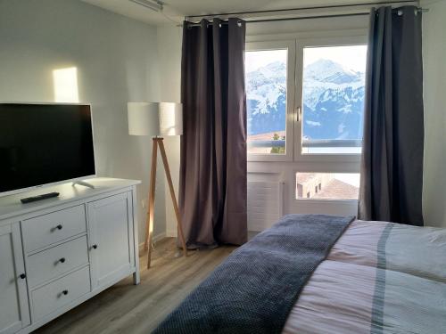 a bedroom with a bed and a television and a window at Swiss Seeblick Apartment mit Hotelanbindung in Beatenberg