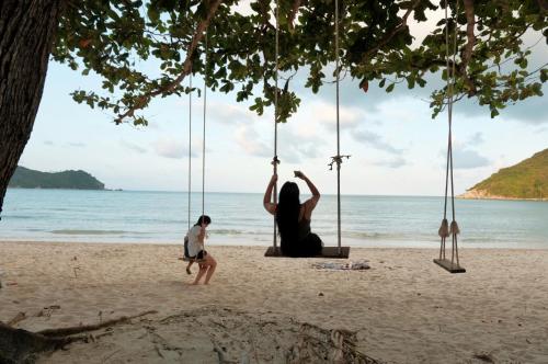 a man and a woman sitting on a swing on the beach at Pen's Bungalow Koh Phangan in Thong Nai Pan Yai