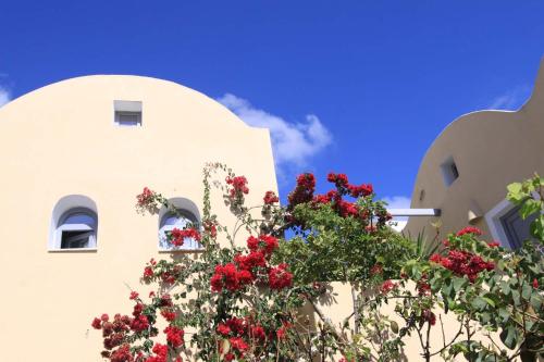 a white building with red flowers in front of it at Ersi Villas in Firostefani