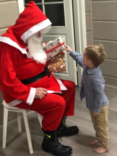 Un niño pequeño señala a un Papá Noel que sostiene un regalo. en Villa Avanto, en Suomenniemi