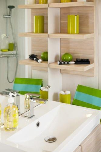 La salle de bains est pourvue d'un lavabo et de 2 chaises vertes. dans l'établissement Camping Le Ventadour, à Meyras