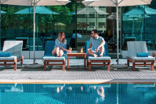 a man and woman sitting in chairs next to a swimming pool at Stella Di Mare Dubai Marina Hotel in Dubai