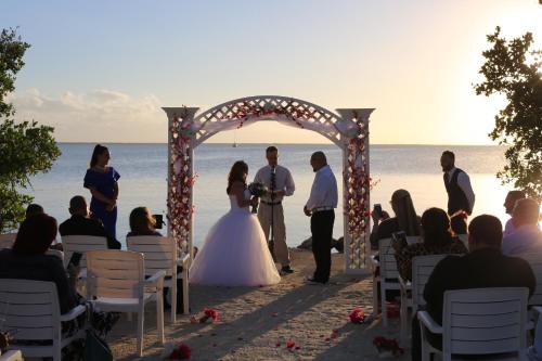 a bride and groom standing under an arch at the beach at Gilbert's Resort in Key Largo