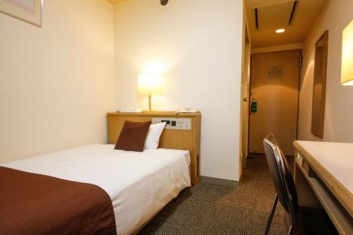 a hotel room with a bed and a desk with a lamp at Shin-Osaka Sunny Stone Hotel in Osaka