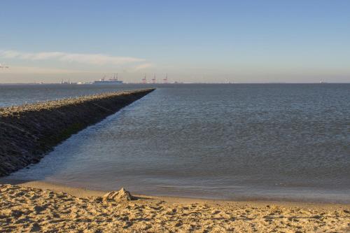 a beach next to the water with a pier at Hotel Am Friesenstrand in Butjadingen