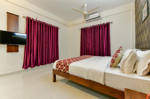 a bedroom with a bed with red curtains and a flat screen tv at Hotel Hilite Inn in Cochin