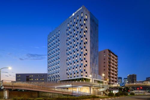un edificio alto con un puente delante de él en hotel MONday Premium TOYOSU en Tokio