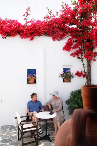 a man and a woman sitting at a table with red flowers at Aegeo Hotel in Chora Folegandros