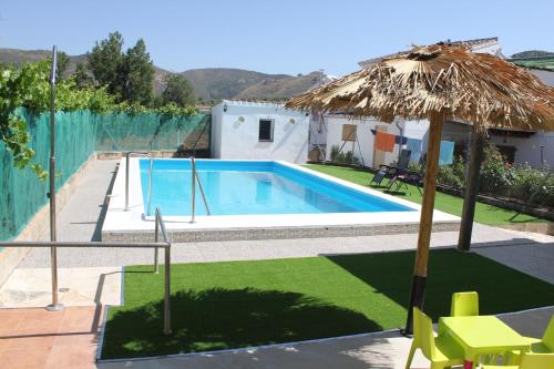 una piscina con ombrellone di paglia, tavolo e sedie di Huerta Espinar - Casa rural con piscina privada ad Archidona