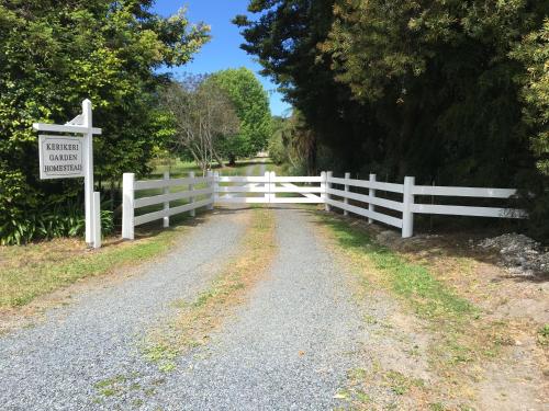 a white fence next to a road with a sign at Kerikeri Garden Homestead in Kerikeri
