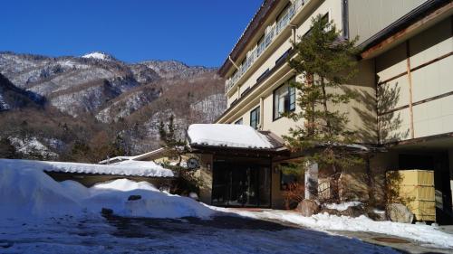 a building with snow on the ground next to a mountain at Tabist Kazeyuki in Takayama