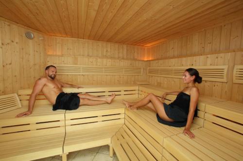 a man and a woman sitting in a sauna at Feldmilla Design Hotel - Wellness & SPA in Campo Tures