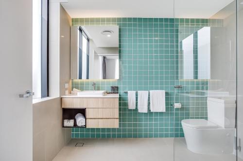 Baño de azulejos verdes con lavabo y aseo en Mantra at Sharks, en Gold Coast
