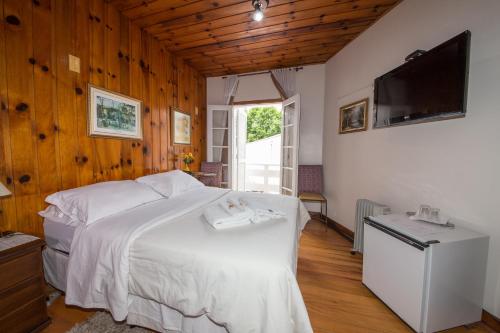 a bedroom with a white bed and a flat screen tv at Siena Hotel in Campos do Jordão