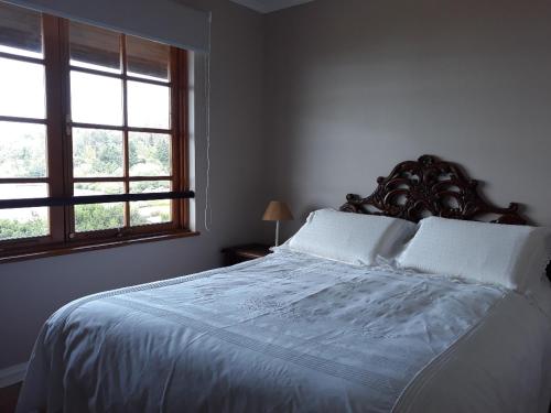 1 dormitorio con 1 cama con sábanas blancas y 2 ventanas en Condominio La Puntilla Km 2 Camino Villarrica Pucon, en Villarrica