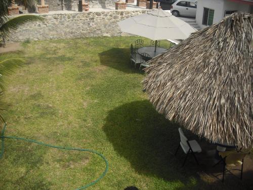 a patio with a grass umbrella and a bench and a table at Hotel Villas del Rey in Chachalacas