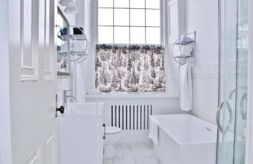 a white bathroom with a toilet and a window at All Suites Whitney Manor in Kingston