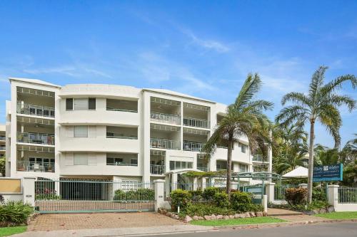 a white building with palm trees in front of it at Trinity Waters Boutique Beachfront in Trinity Beach