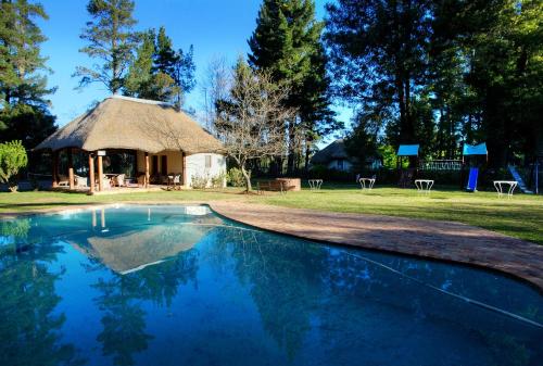 a swimming pool in front of a thatched house at Hogsback Arminel Hotel in Hogsback