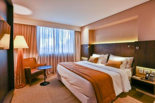 a hotel room with a large bed and a chair at Transamerica Collection Goiania in Goiânia