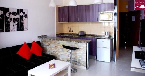 a living room with a black couch and a kitchen at Apartamentos las Dunas in Playa del Ingles