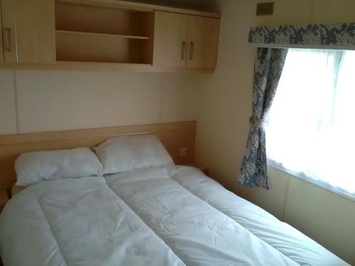 a white bed in a bedroom with a window at Caravan hire Winthorpe Skegness in Skegness