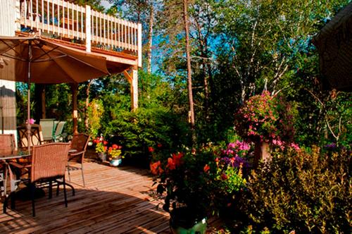 a deck with a table and chairs and flowers at Gîte au Pied du Courant de Gilbert Desjardins in Mont-Laurier