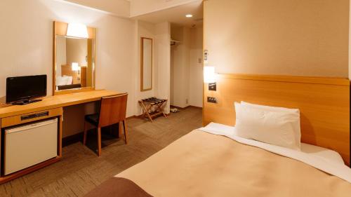 a hotel room with a bed and a desk with a television at Hachinohe Park Hotel in Hachinohe