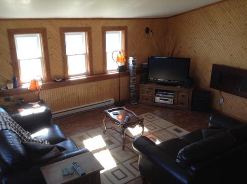 a living room with two couches and a flat screen tv at Gîte Au Coin De La Berge in Perce