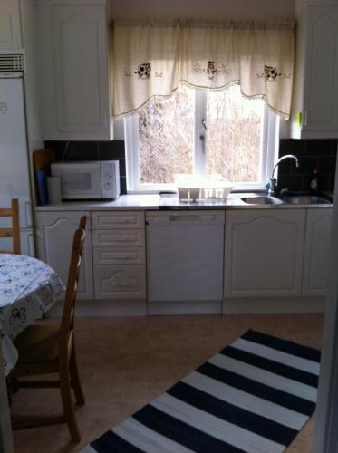 uma cozinha com armários brancos, um lavatório e uma janela em Odensvi Vandrarhem em Odensvi