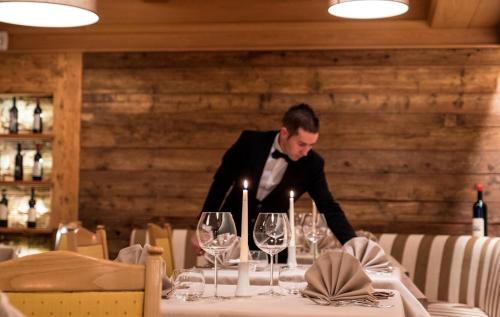 a man in a tuxedo sitting at a table with wine glasses at La Roccia Wellness Hotel in Cavalese