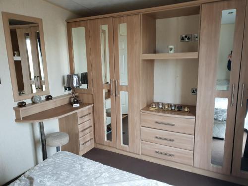 a bedroom with a large wooden cabinet with a mirror at Park Home at Golden Sands Holiday Park in Foryd