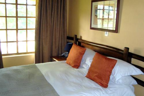 a bedroom with a bed with two orange pillows at Riverside Lodge & Conference Center in Aliwal North
