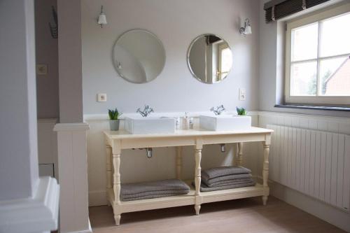 uma casa de banho com dois lavatórios e dois espelhos na parede em 'Hof der Heerlijckheid' em Borgloon