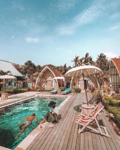 two people sitting on a wooden deck near a swimming pool at La Roja Bungalows in Nusa Penida