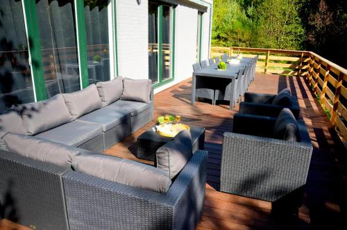 a wooden deck with couches and a table and a table at Villa Dakota - jacuzzi, zwembad, playstation in Durbuy