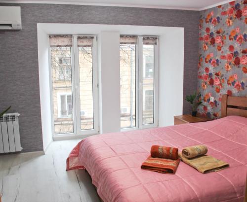 a bedroom with a pink bed with two towels and windows at City Centre Apartment in Odesa