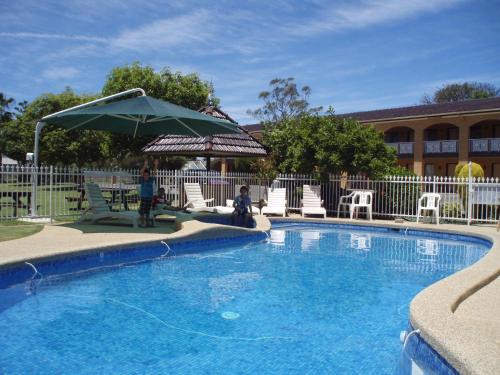 a swimming pool with an umbrella and chairs and a table at Lakeview Motel in Yarrawonga