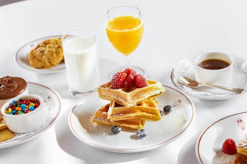 a table topped with plates of waffles and a glass of orange juice at Mr C Beverly Hills in Los Angeles