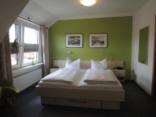 a bedroom with green walls and a bed with white pillows at Hotel Ostfriesland garni in Norden