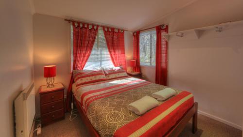 a bedroom with a bed with red curtains and a window at Kosciusko Tourist Park in Jindabyne