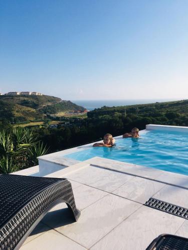 two people in a swimming pool with the ocean in the background at Casa Tazmin in Santo Isidoro